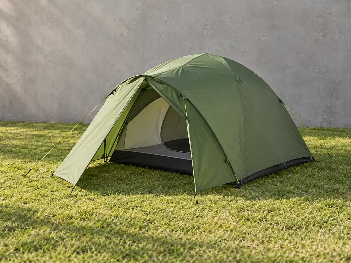 Two-person green dome tent with a rain fly and front vestibule, pitched on grass